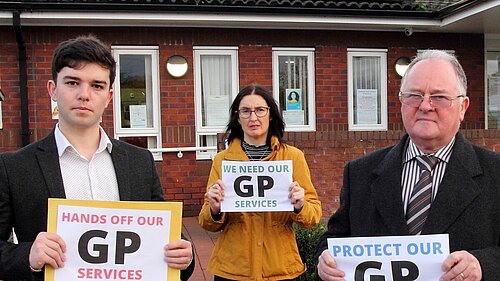 Alex Wagner, Mary Davies & Bernie Bentick outside GP Surgery holding Hands off GP Services